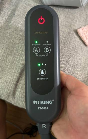 Hand holding a Fit King FT-009A limb  massager distant    with mode   and strength  settings displayed