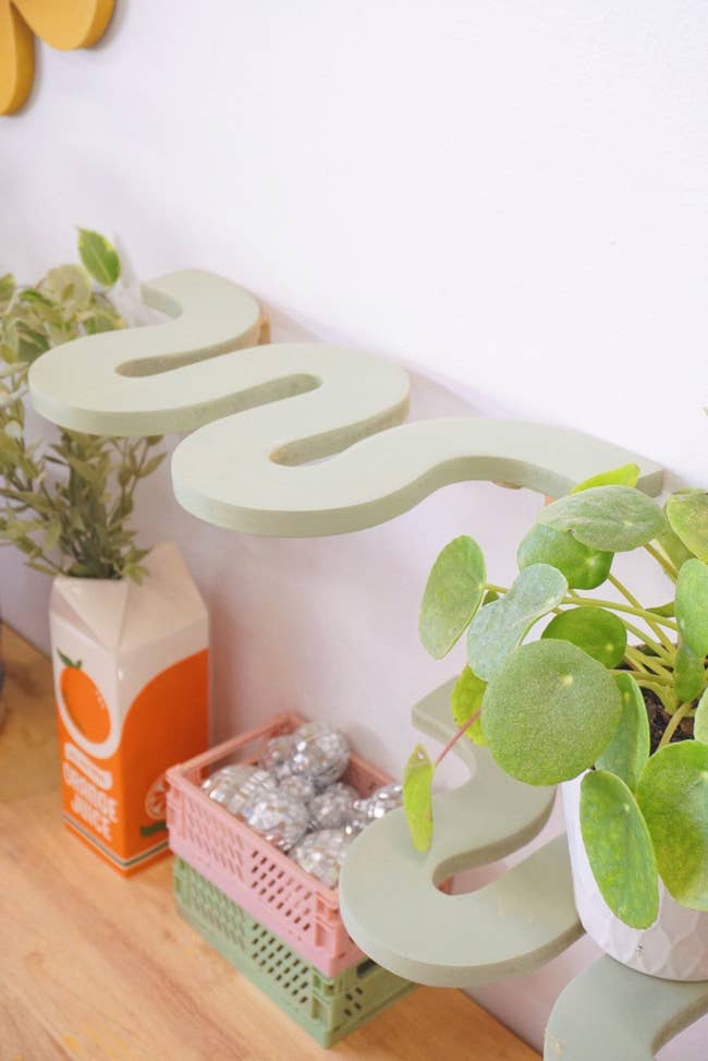 Potted plant next to modern cursive-style decor with orange juice carton and crate of silver ornaments on a shelf