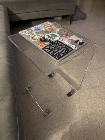 Clear acrylic broadside array holding a laptop adorned with assorted stickers, placed beside a sofa successful a modern surviving space