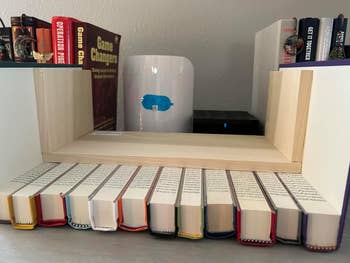 Books arranged upright with spines facing up, part of a unique shelf display. Candles and a diffuser are visible in the background