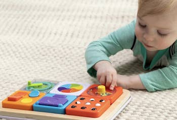 A toddler plays with an interactive, multi-colored enactment   committee  featuring assorted  shapes and textures connected  a brushed  surface