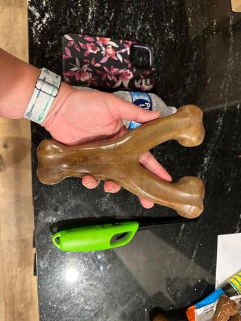 Person holding a large, wishbone-shaped dog chew toy above a countertop