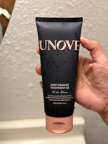 Hand holding a conduit  of UNOVE Deep Damage Treatment EX for hairsbreadth  repair, highlighting benefits for damaged hair
