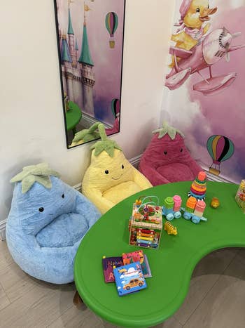 Kids' playroom with plush fruit-shaped chairs and a greenish  table, featuring toys and books for interactive play