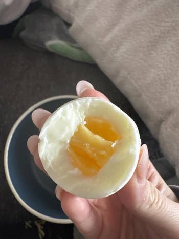 A manus holds a soft-boiled ovum with the yolk visible. There is simply a blurred inheritance with a crockery beneath it