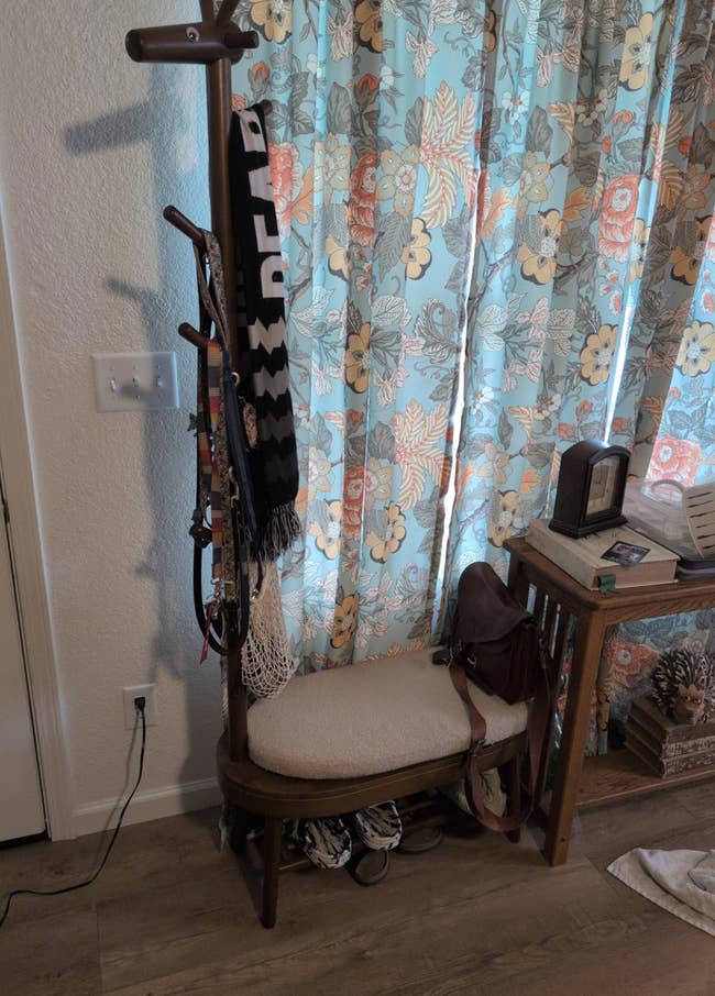 A cozy entryway with a wooden bench, patterned curtain, and a coat rack holding scarves and hats. Shoes and a bag are placed underneath