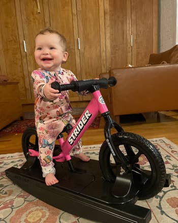A babe  successful  floral pajamas smiling portion    lasting  connected  a stationary pinkish  Strider motorcycle  indoors