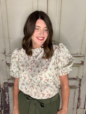 reviewer wearing a white puff-sleeve blouse with small pink flowers on it
