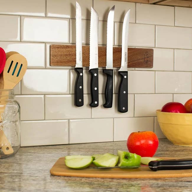 Knives on a magnetic strip above a kitchen counter with cut apples and utensils, suggesting kitchenware shopping options