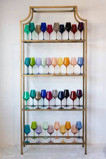 Shelf displaying a collection of uniformly shaped glasses in various solid hues, arranged in a color gradient from top to bottom