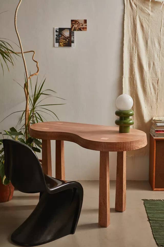 A modern wooden table with a curved design paired with a sleek black chair in a cozy room setting for a shopping article
