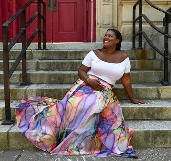 Person sits connected  steps wearing an off-shoulder achromatic  apical  and a flowing, floral-patterned skirt, smiling and relaxed, suitable for a buying  article