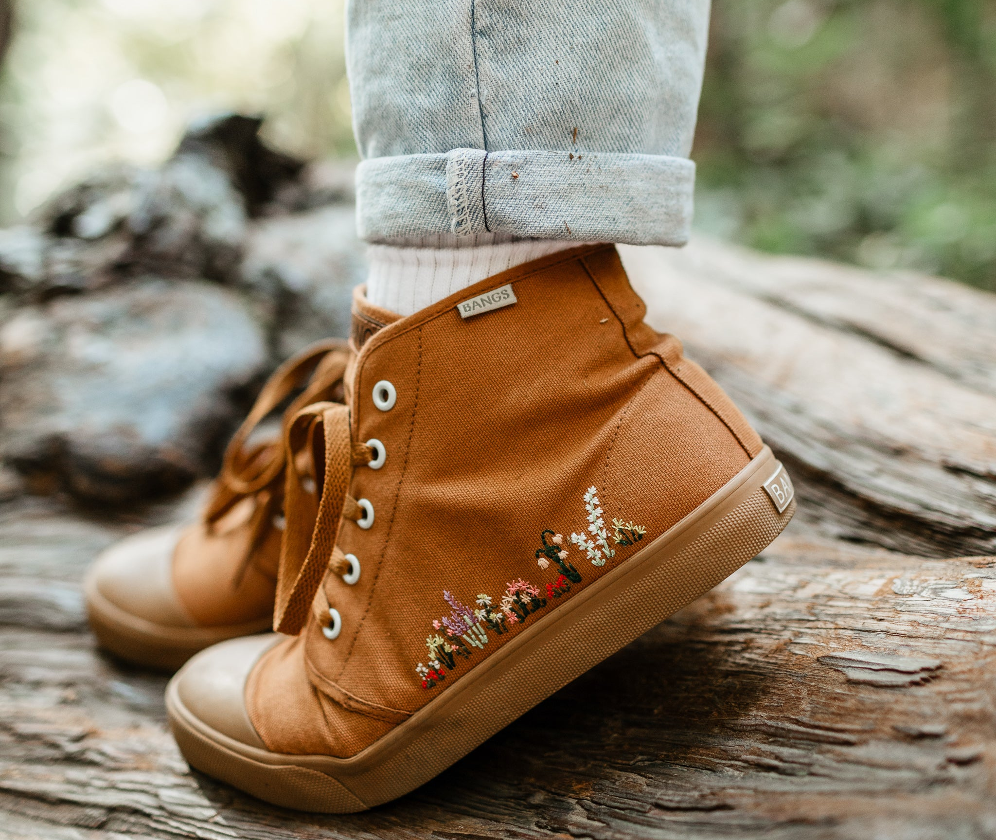 a model wearing a tan canvas hightop sneaker with floral embroidery along the side 
