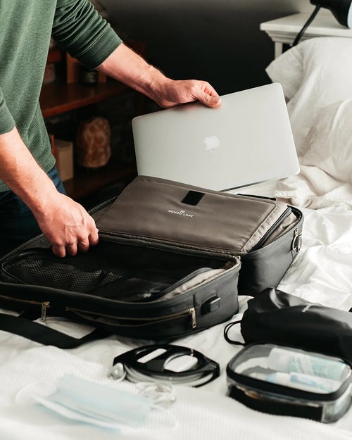 model sliding a laptop into the black bag's laptop pouch