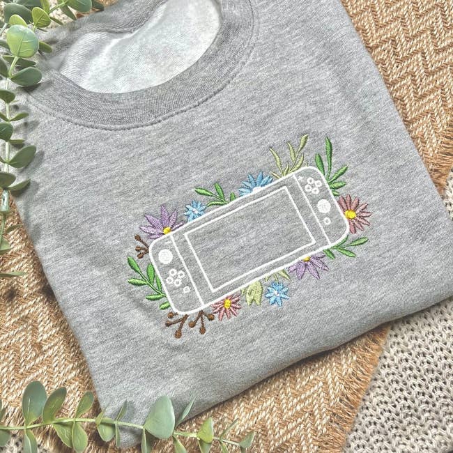 a gray sweatshirt with an embroidered flowers around an outline of a nintendo switch console