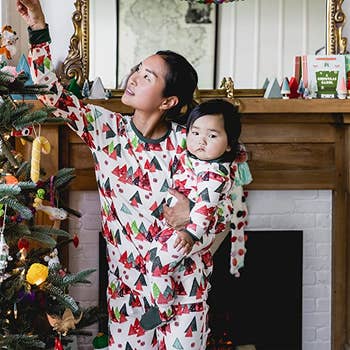 a woman and a baby in matching holiday pajamas decorating a tree