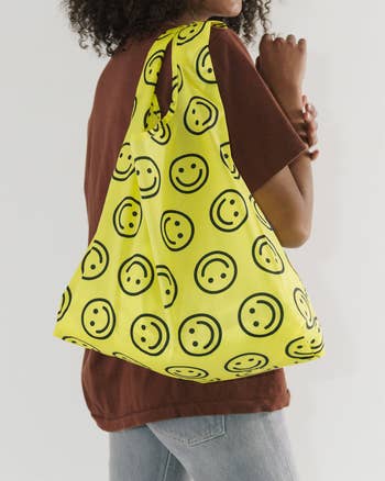 Person carrying a large yellow tote bag with smiley face pattern, ideal for a cheerful accessory