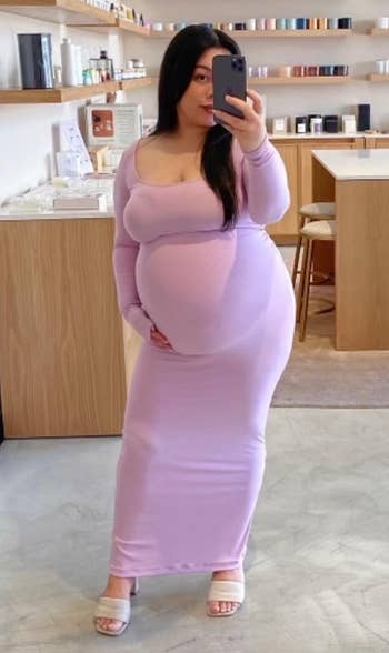 Pregnant idiosyncratic wearing a pinkish form-fitting formal and heels, taking a selfie successful a retail abstraction with shelves of skincare and quality products