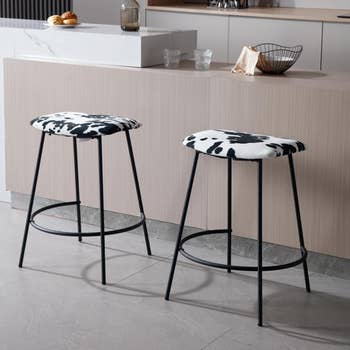 Two bar stools with cow print seats against a kitchen island, showcasing modern home decor.
