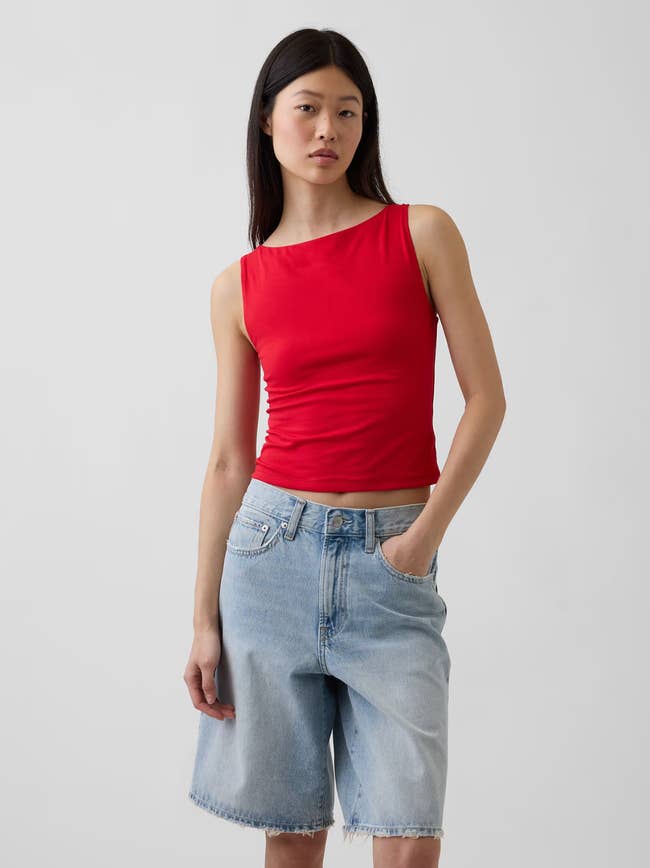 A exemplary  wearing a sleeveless reddish  apical  and airy  denim knee-length shorts poses with 1  manus  successful  her pocket