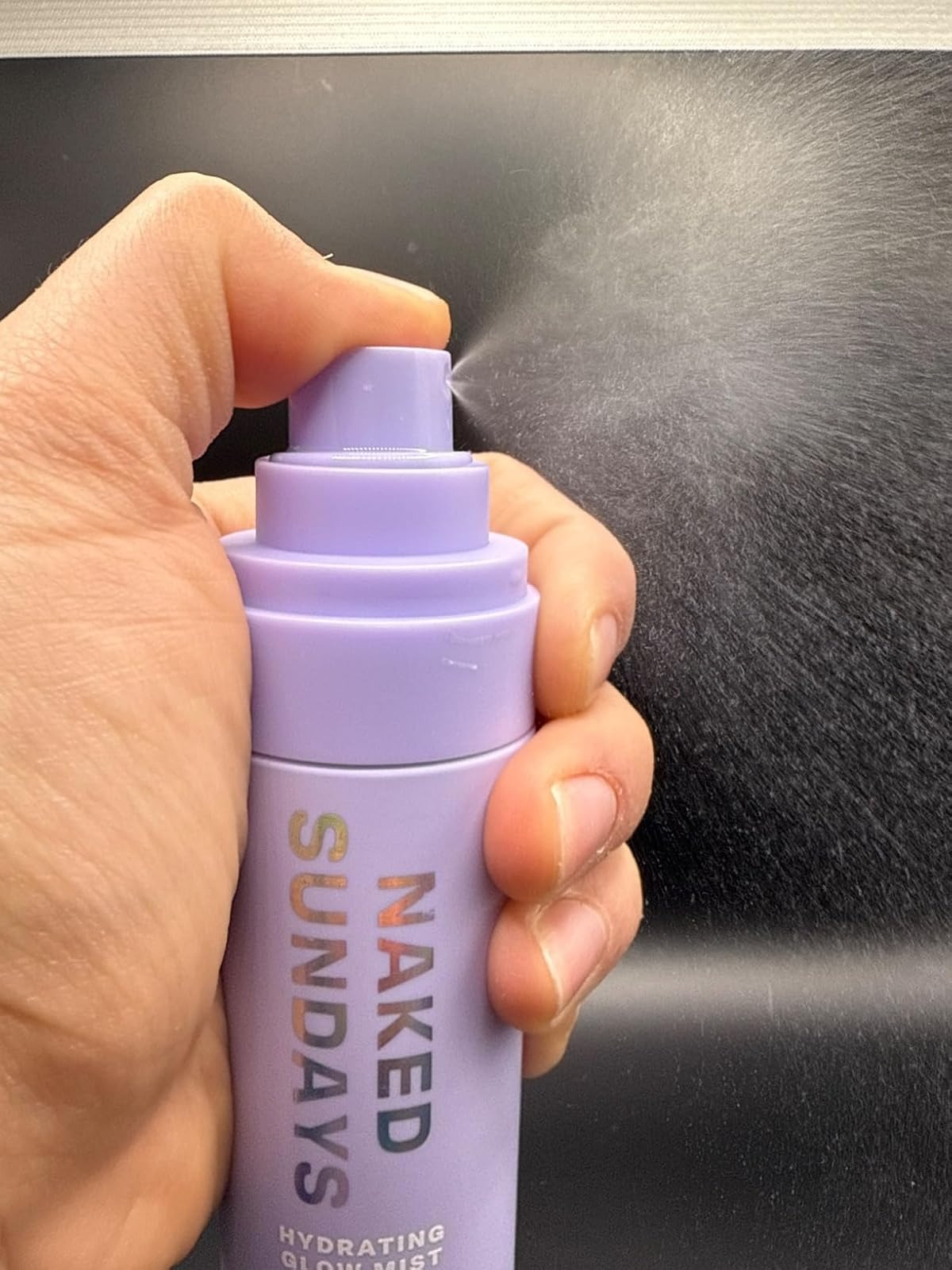 A manus  holds a Naked Sundays hydrating mist bottle, spraying a good  mist