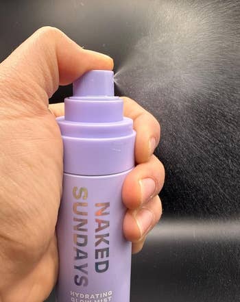 A manus holds a Naked Sundays hydrating mist bottle, spraying a good mist