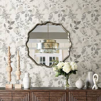 the grey botanical wallpaper on a wall behind a credenza and mirror