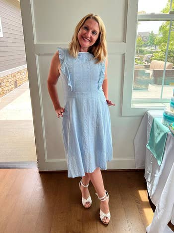reviewer in a light blue midi dress with ruffle sleeves and white sandals stands