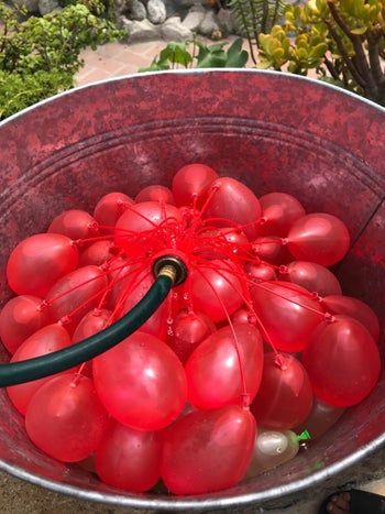 reviewer image of a hose filling a bunch of red self-sealing water balloons
