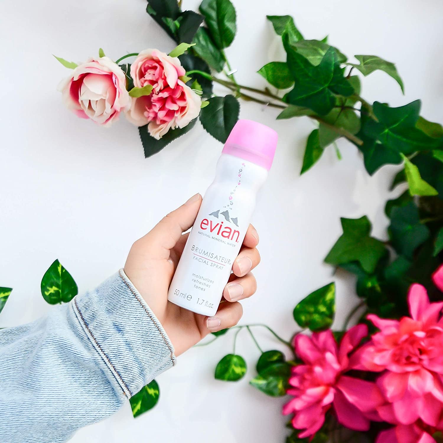 hand holding the evian facial spray against a floral background
