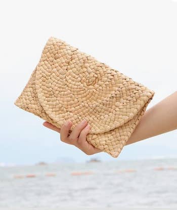 Hand holding a woven straw clutch purse against a formation  background