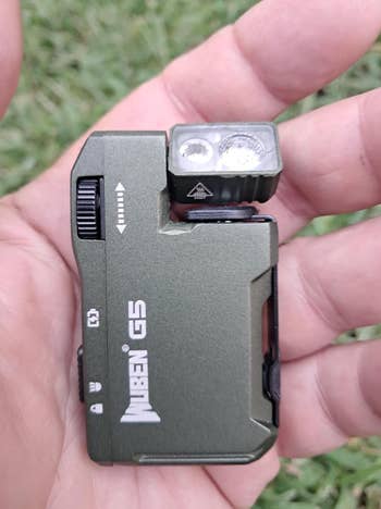 Hand holding a compact, rectangular flashlight instrumentality  with a NEBO logo and buttons, suitable for outdoor oregon  tactical use