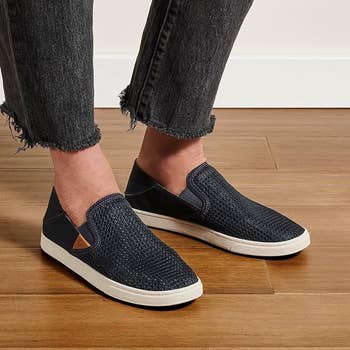 A pair of slip-on casual shoes being modeled with frayed hem jeans on a wooden floor background