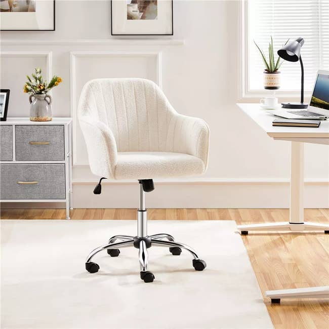 Office chair with padded seat and chrome base on wheels, placed in a modern home office setup with desk and decor accents