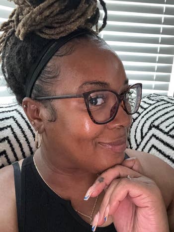 Person with glasses and braided hairsbreadth  poses smiling indoors, wearing a sleeveless apical  and hoop earrings