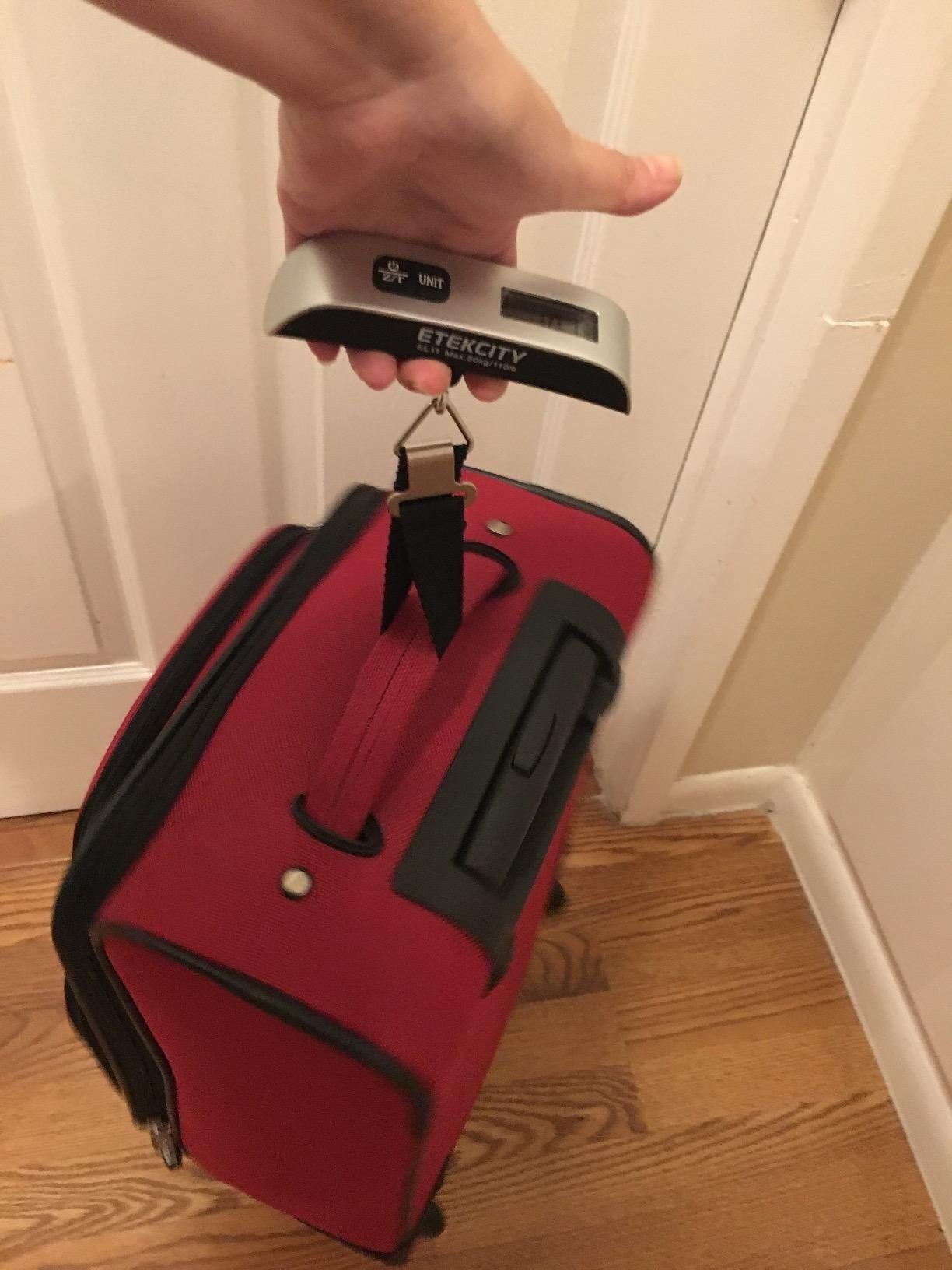the reviewer using the scale to weigh a red suitcase