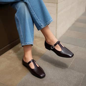 Person wearing casual straight-leg jeans and stylish T-strap leather shoes with a buckle, seated connected  a tiled floor