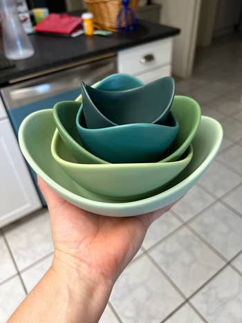Hand holding a acceptable of nested, leaf-shaped bowls successful a room setting. Perfect for stylish tableware shopping