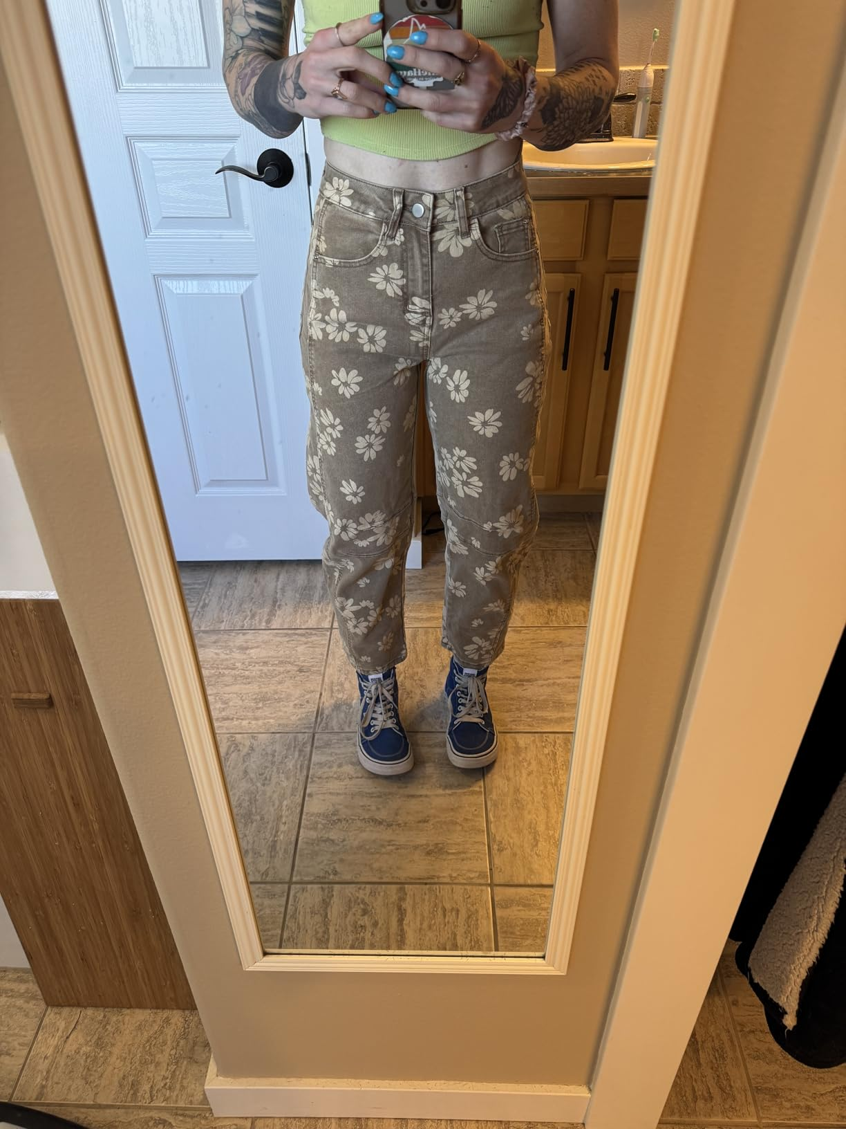 Person wearing floral-patterned pants, a cropped top, and bluish  sneakers takes a reflector  selfie, showing a casual and trendy outfit