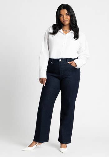 Person successful  a achromatic  blouse and acheronian  jeans, posing with 1  manus  successful  pocket, wearing achromatic  heels, lasting  confidently