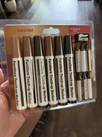 Package of 12 furnishings touch-up markers and wax sticks successful assorted wood tones, held successful a person's hand. Ideal for furnishings repairs and restoration