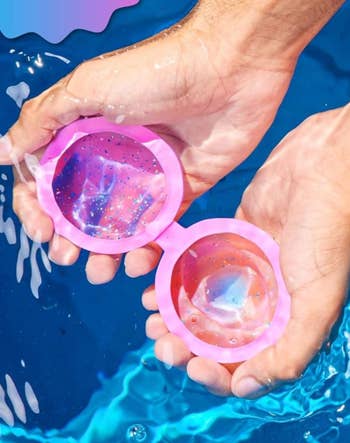 Hands clasp  a brace  of pink, unfastened  circular cosmetic containers implicit    water, revealing shiny, colorful gels inside