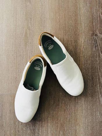 Two achromatic  slip-on shoes connected  a woody  floor