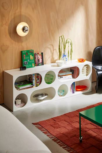 Modern living room with a minimalist bookshelf, display of books and decor items, and a chic light fixture, featured in a shopping article