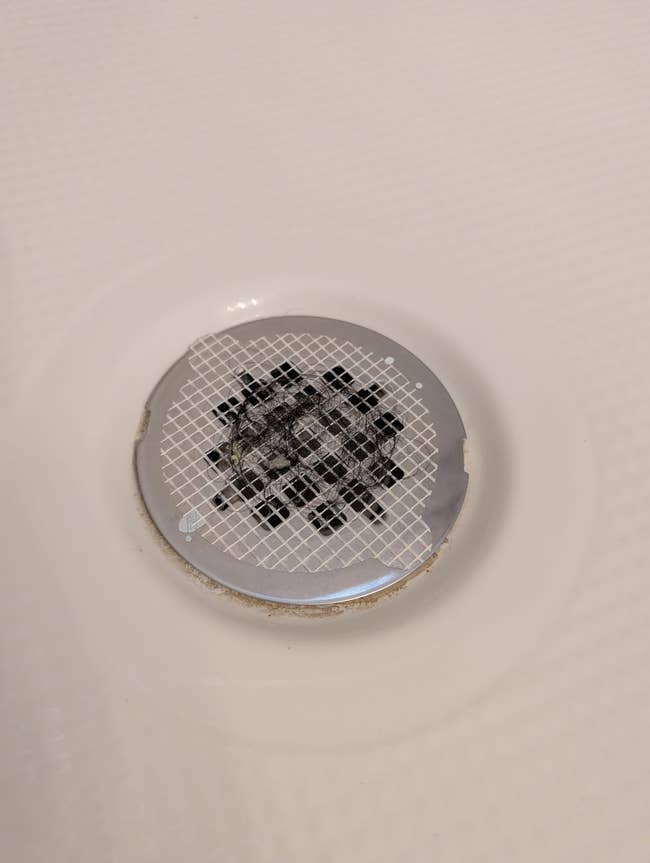 Shower drain screen with a grid signifier shows signs of deterioration and mineral buildup