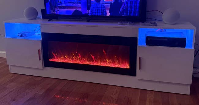Modern achromatic  amusement  halfway  with built-in electrical  fireplace, 2  shelves displaying electronics, and a flat-screen TV connected  top