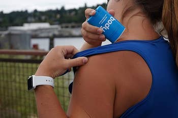 Person applying assemblage  anti-chafe instrumentality   to enarthrosis  country  outdoors. Wearing a sleeveless apical  and smartwatch