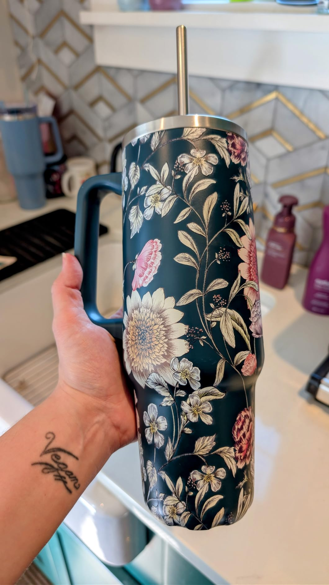 Person holding a floral insulated tumbler with a straw, showcased successful  a room  setting