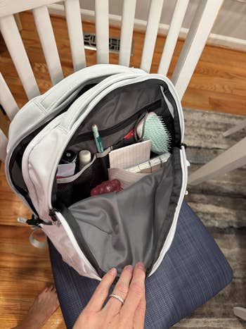 Open backpack connected  seat  showing organized compartments with toiletries, notebook, pen, and a brush. Hand holding the bag, implying packing oregon  organizing