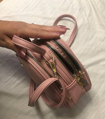 a reviewer opening the three compartments of the pink crossbody bag